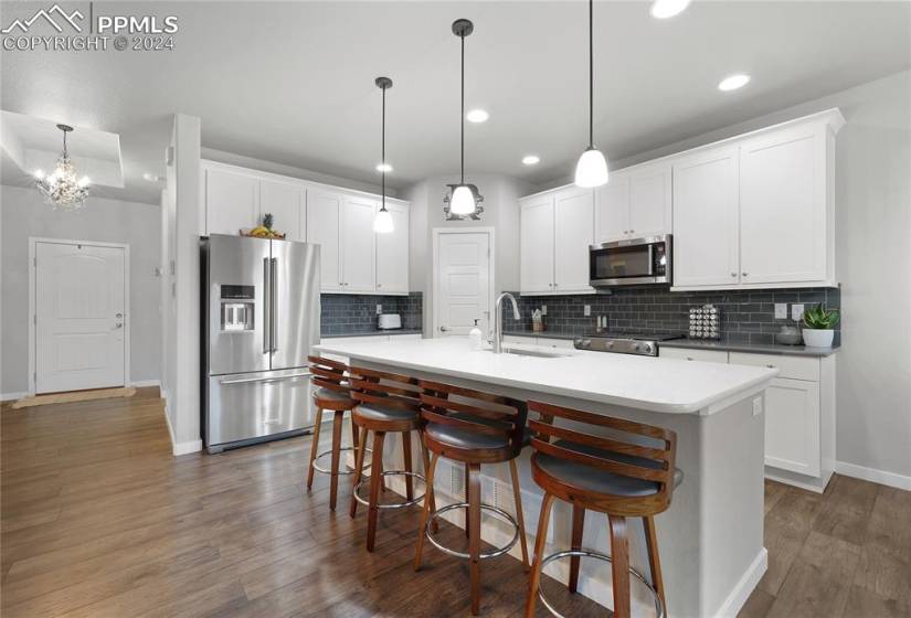 Kitchen with tasteful backsplash, dark hardwood / wood-style flooring, a kitchen island with sink, appliances with stainless steel finishes, and hanging light fixtures