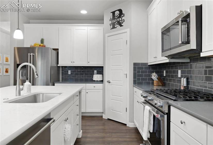Kitchen with white cabinets, high quality appliances, tasteful backsplash, pendant lighting, and dark wood-type flooring