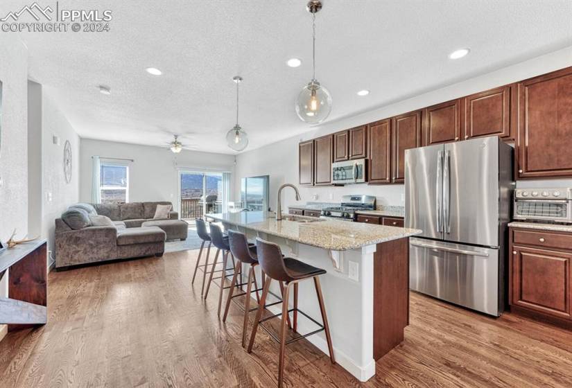 Kitchen with hardwood floors, an island with sink, a kitchen bar, decorative light fixtures, and stainless steel appliances