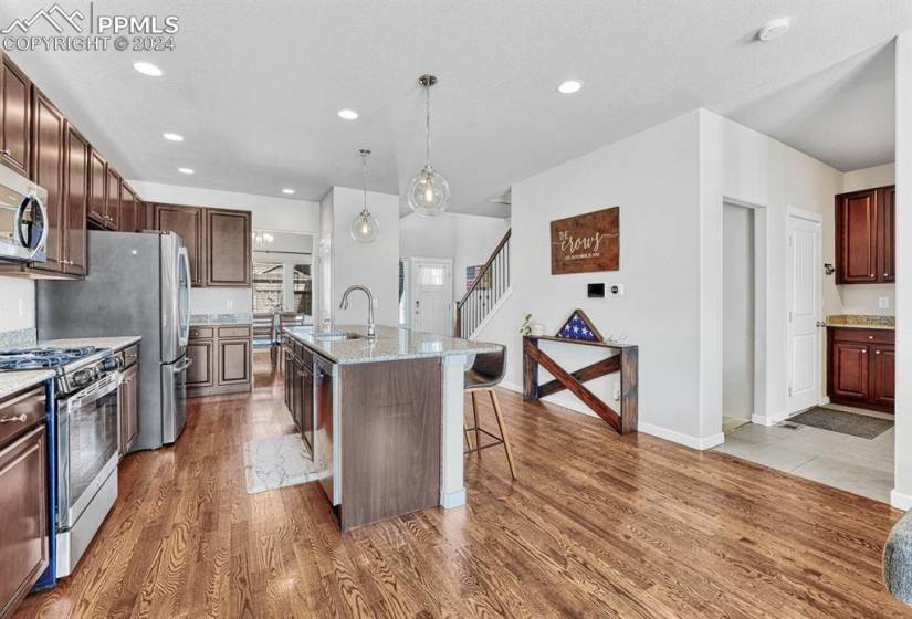 Kitchen featuring a center island with sink, light hardwood floors, a kitchen breakfast bar, hanging light fixtures, and stainless steel appliances