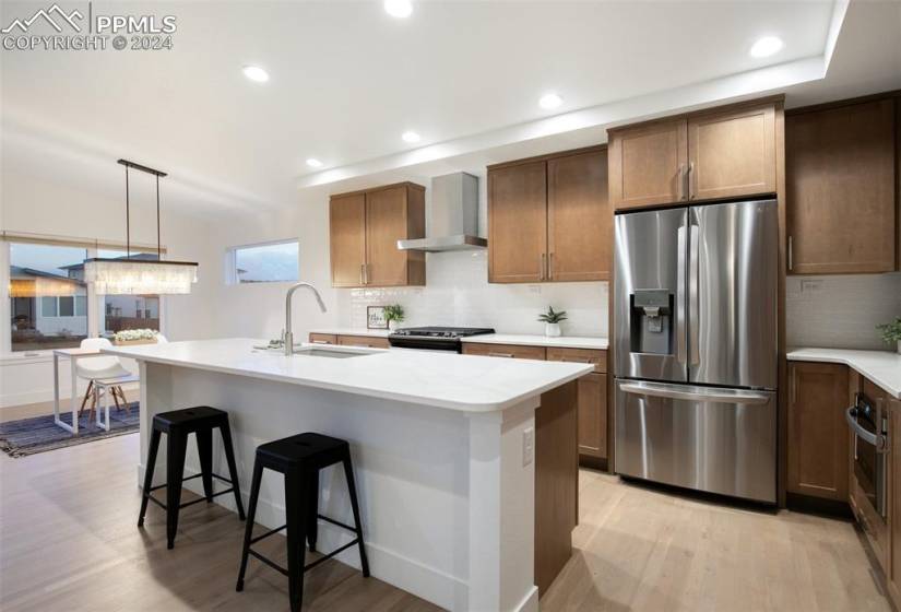 Kitchen featuring wall chimney range hood, decorative light fixtures, backsplash, light hardwood / wood-style flooring, and stainless steel appliances