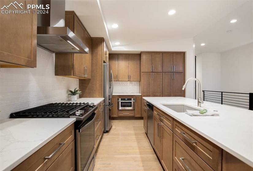 Kitchen featuring sink, wall chimney range hood, light hardwood / wood-style floors, backsplash, and stainless steel appliances