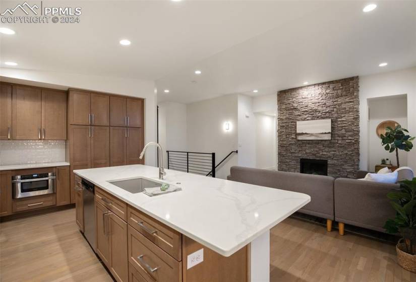 Kitchen with a fireplace, a kitchen island with sink, sink, appliances with stainless steel finishes, and light wood-type flooring