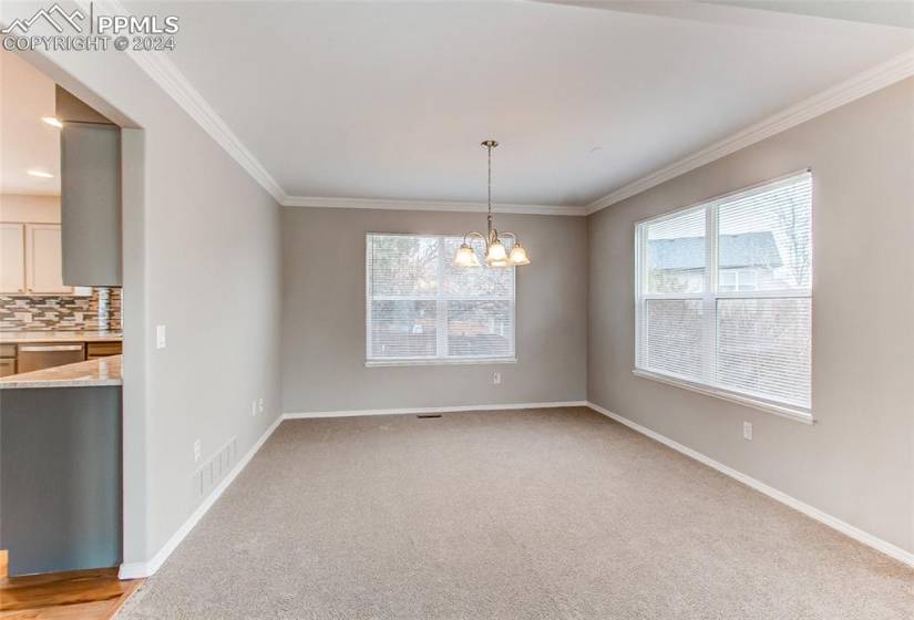 Spare room with a chandelier, light colored carpet, and crown molding