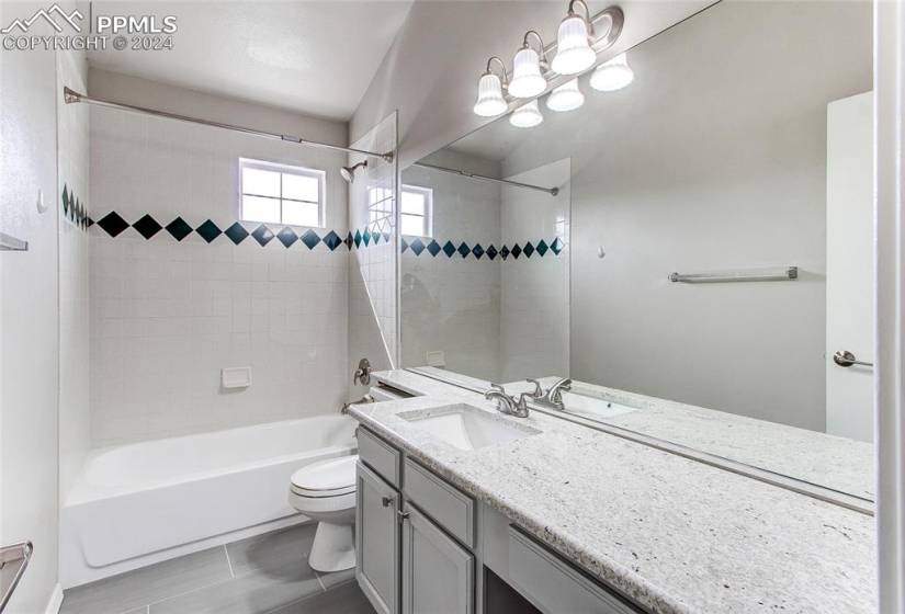 Full bathroom with oversized vanity, toilet, tiled shower / bath combo, and tile floors