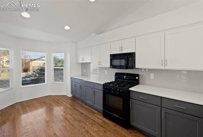 Kitchen with backsplash, vaulted ceiling, white cabinets, dark hardwood / wood-style floors, and black appliances