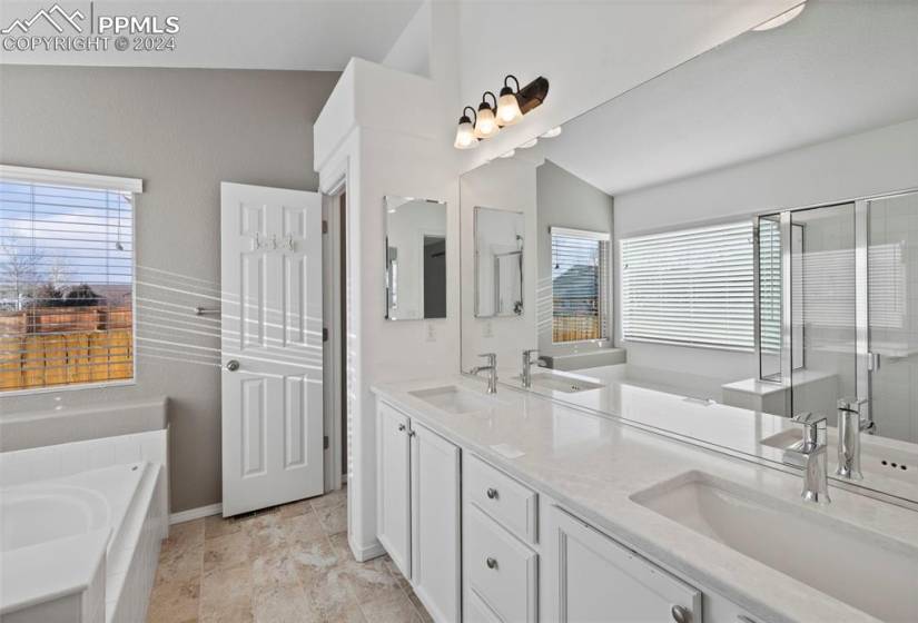 Bathroom with lofted ceiling, dual sinks, vanity with extensive cabinet space, a bathing tub, and a healthy amount of sunlight