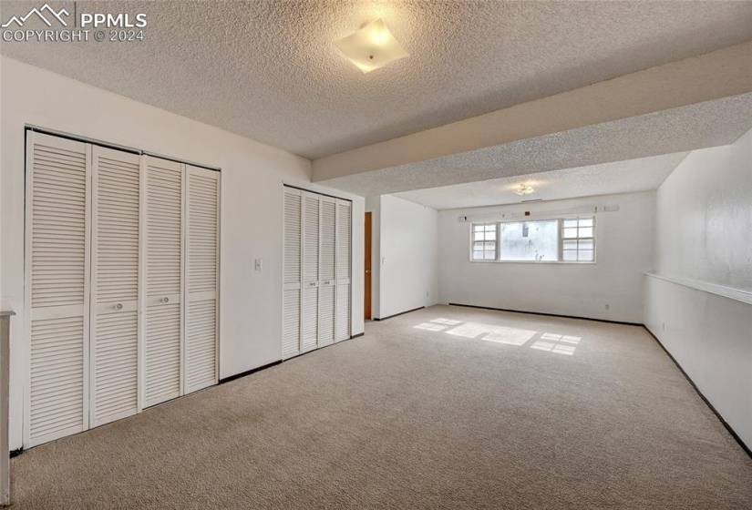 Unfurnished bedroom featuring light colored carpet, a textured ceiling, and two closets