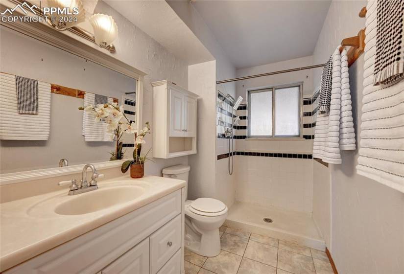 Bathroom with tiled shower, toilet, large vanity, and tile floors