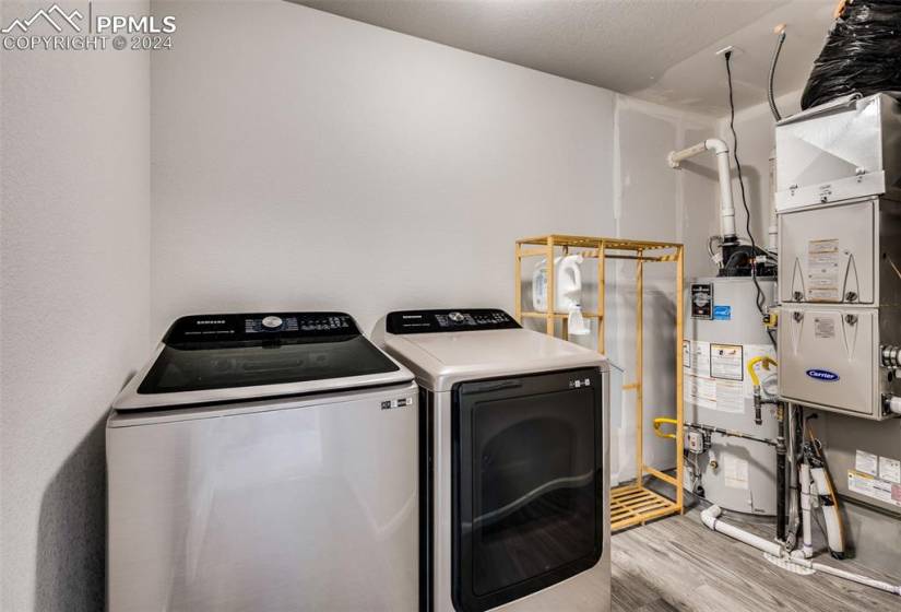 Clothes washing area with light wood-type flooring, gas water heater, and washer and dryer