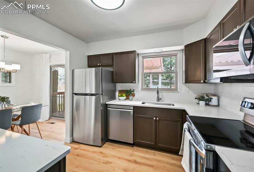 Kitchen with a notable chandelier, sink, appliances with stainless steel finishes, light hardwood / wood-style floors, and hanging light fixtures