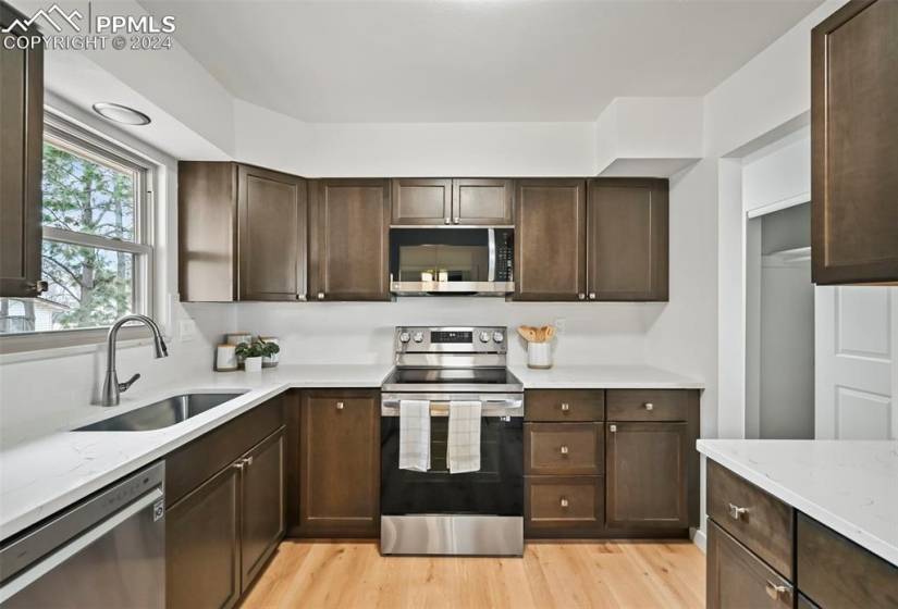 Kitchen featuring appliances with stainless steel finishes, light hardwood / wood-style flooring, dark brown cabinets, and sink