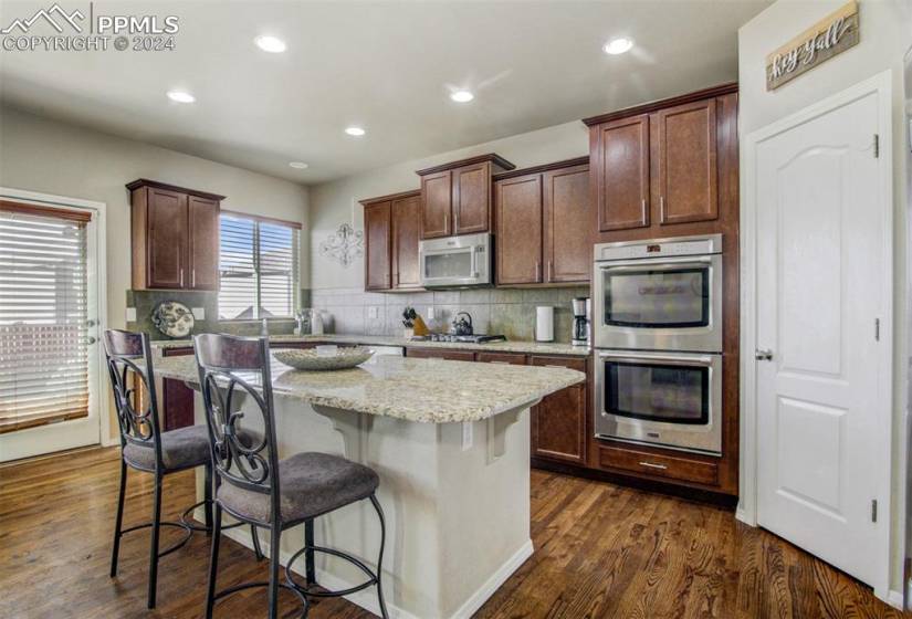 Kitchen featuring dark wood-type flooring, appliances with stainless steel finishes, a kitchen island, and backsplash