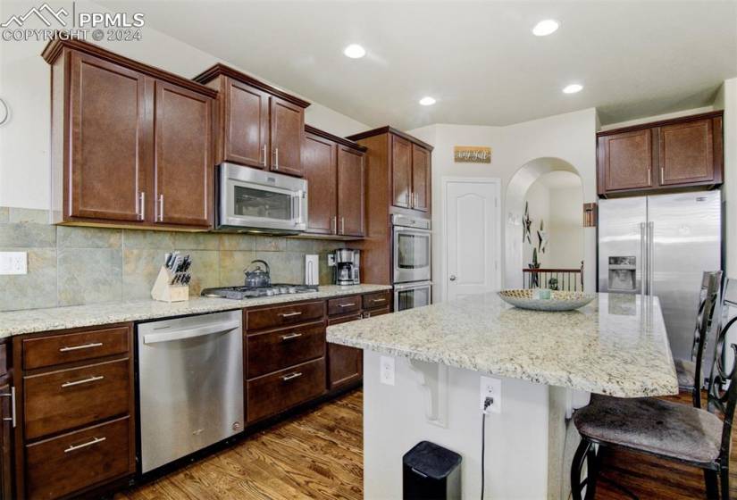 Kitchen with dark hardwood / wood-style floors, stainless steel appliances, light stone counters, and a breakfast bar area