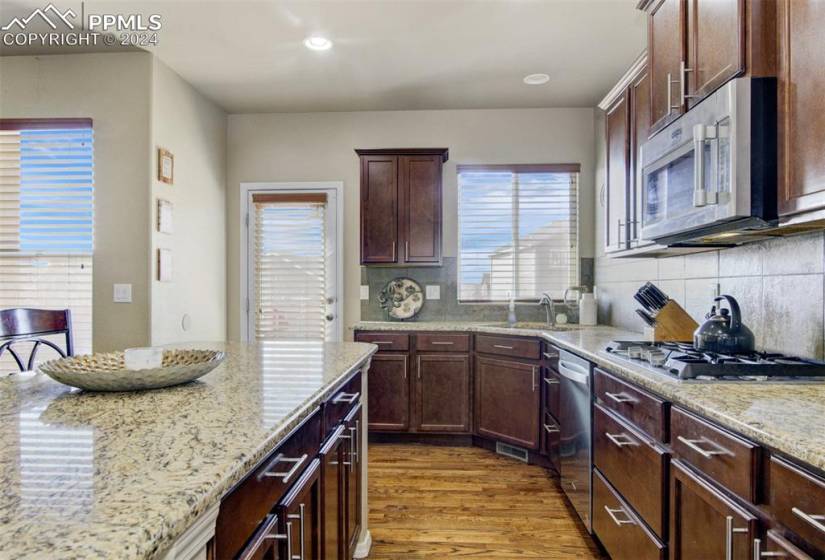 Kitchen with appliances with stainless steel finishes, tasteful backsplash, light hardwood / wood-style floors, and light stone counters