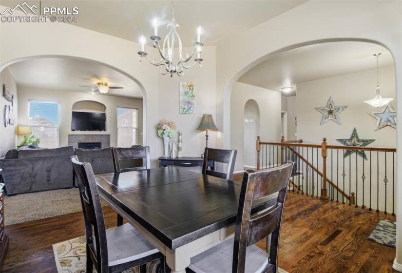 Dining space with dark hardwood / wood-style flooring, ceiling fan with notable chandelier, and a tiled fireplace