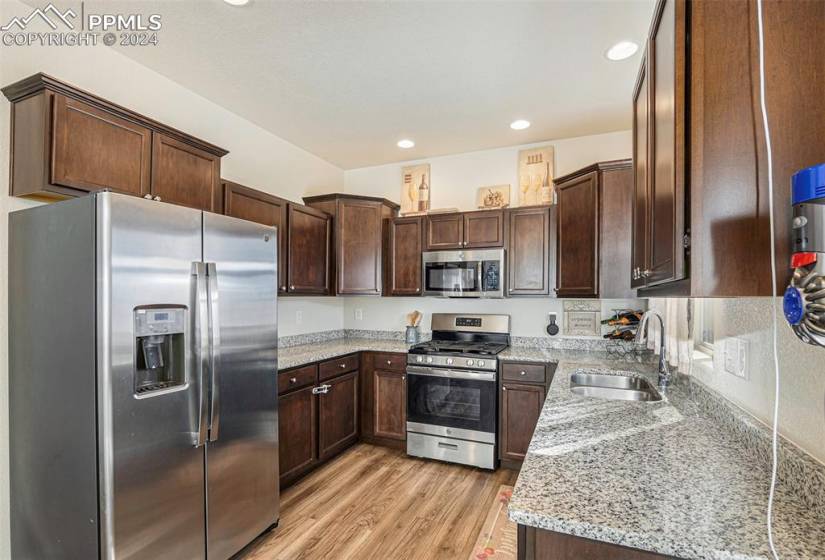Kitchen featuring sink, light hardwood / wood-style floors, appliances with stainless steel finishes, light stone counters, and dark brown cabinets