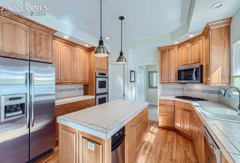 Kitchen featuring a kitchen island, appliances with stainless steel finishes, hardwood flooring, backsplash, and tile countertops