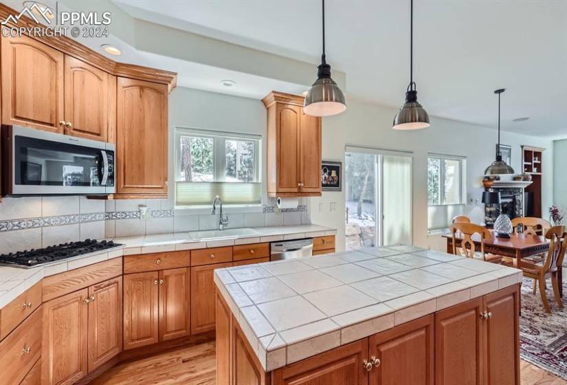 Kitchen featuring sink, tile countertops, hardwood flooring, hanging light fixtures, and stainless steel appliances