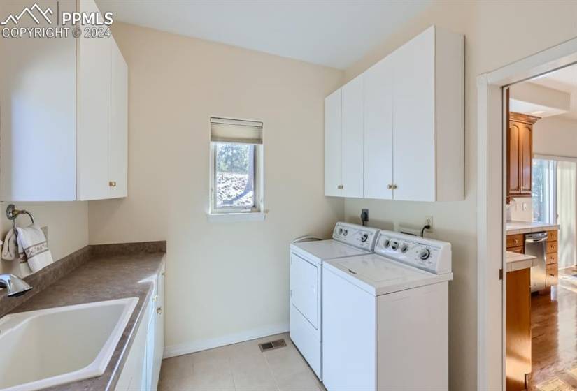 Laundry room with sink, hookup for a gas or electric dryer, tile floors, and storage cabinets