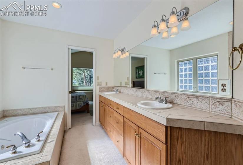 Bathroom with dual sinks, tiled Jacuzzi tub, and vanity with extensive cabinet space