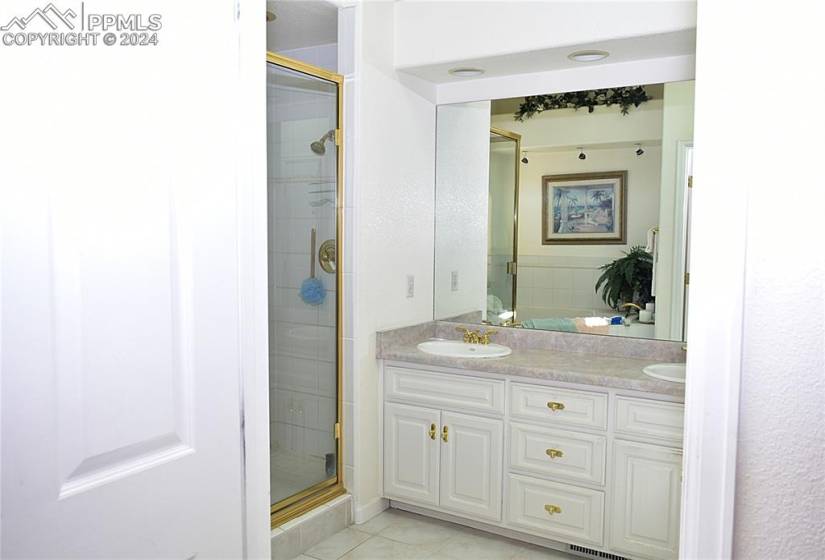 Bathroom featuring vanity with extensive cabinet space, an enclosed shower, tile floors, and double sink