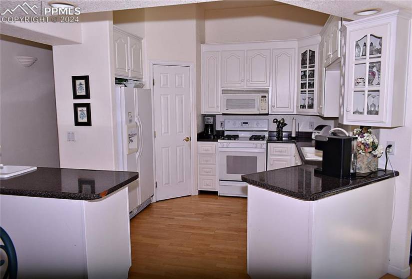 Kitchen with white cabinetry, white appliances, light hardwood / wood-style floors, and kitchen peninsula