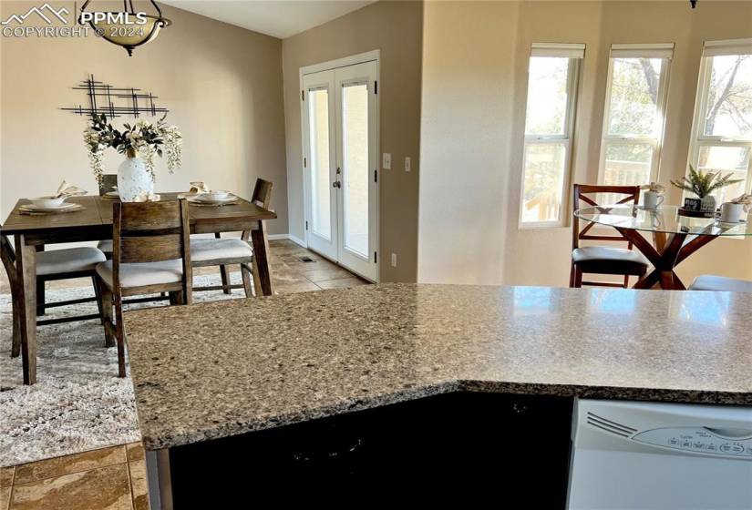 Kitchen with white dishwasher, light tile flooring, light stone counters, french doors, and an island with sink