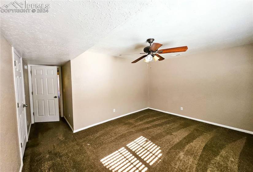 Unfurnished room featuring dark colored carpet, a textured ceiling, and ceiling fan