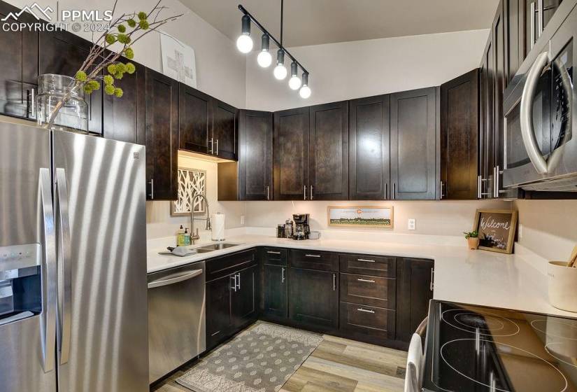 Kitchen featuring sink, dark brown cabinetry, track lighting, appliances with stainless steel finishes, and light hardwood / wood-style flooring