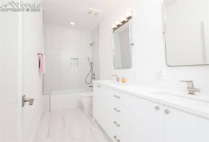 Full bathroom with tile floors, toilet, tiled shower / bath combo, and dual bowl vanity