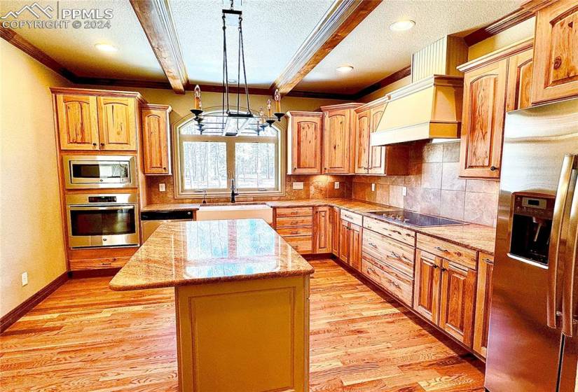 Kitchen with custom exhaust hood, stainless steel appliances, light hardwood / wood-style floors, decorative light fixtures, and a center island