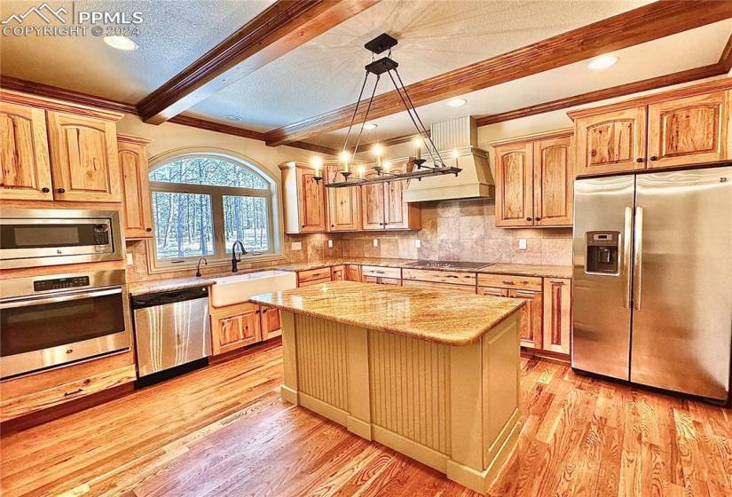 Kitchen with custom exhaust hood, appliances with stainless steel finishes, sink, light wood-type flooring, and a center island
