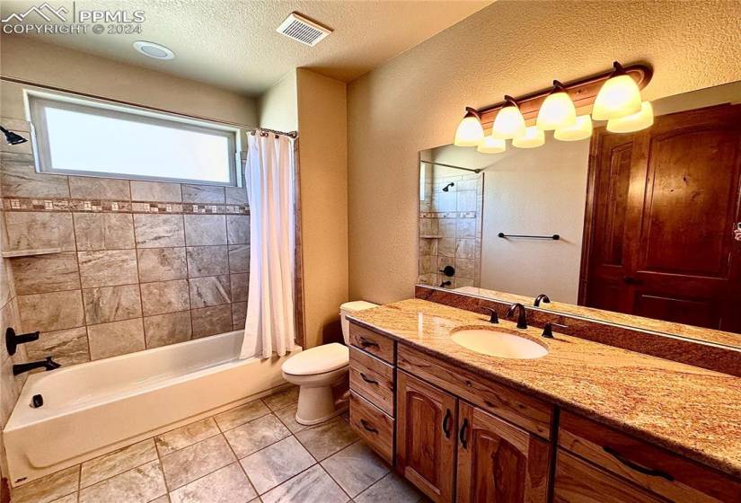 Full bathroom with tile floors, shower / bath combo with shower curtain, large vanity, and toilet