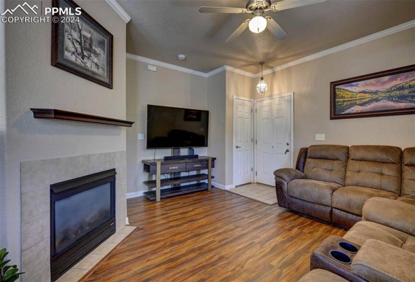 Living room with ornamental molding, a tiled fireplace, ceiling fan, and hardwood / wood-style floors