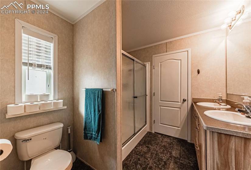 Bathroom featuring dual sinks, a shower with door, large vanity, and toilet