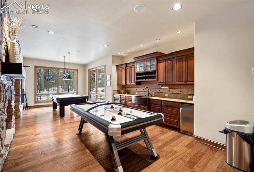 Rec room with billiards, a stone fireplace, light hardwood / wood-style floors, and kitchen area