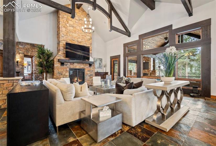 Large great room featuring a notable chandelier, high vaulted ceiling, a stone fireplace, and beam ceiling
