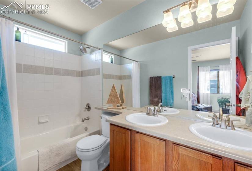 Primary bathroom featuring shower / bathtub combination with curtain, dual sinks, toilet, and plenty of natural light