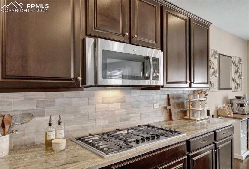 Kitchen featuring appliances with stainless steel finishes, backsplash, dark brown cabinets, and light stone countertops