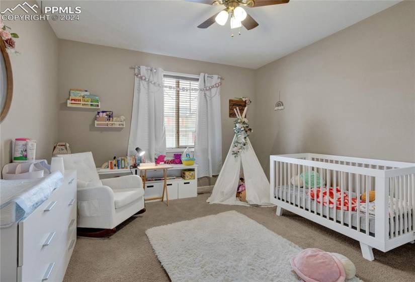 Bedroom with a crib, light carpet, and ceiling fan