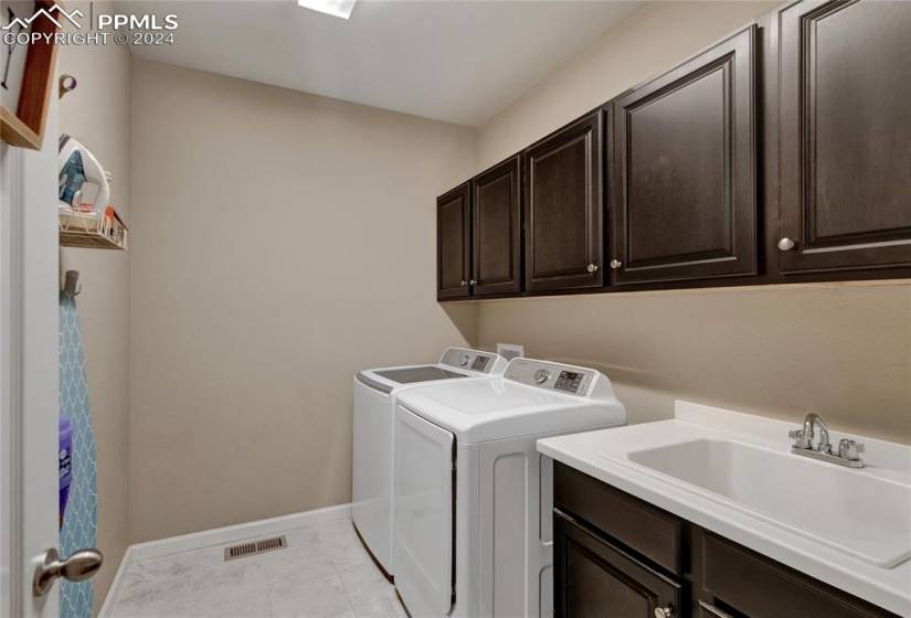 Laundry area featuring cabinets, light tile floors, sink, and washing machine and clothes dryer. Located on the main level