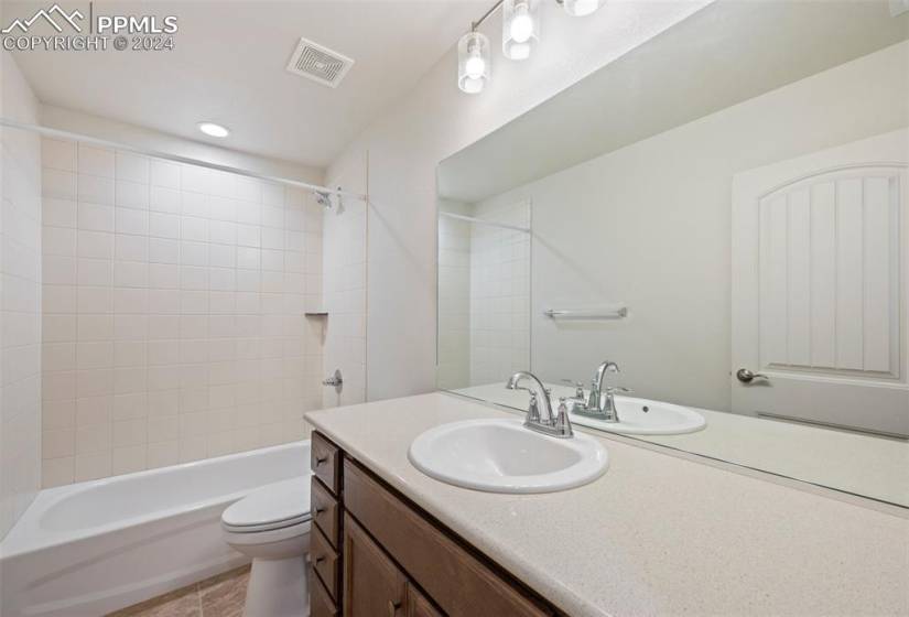 Full bathroom featuring toilet, vanity with extensive cabinet space, tiled shower / bath, and tile floors