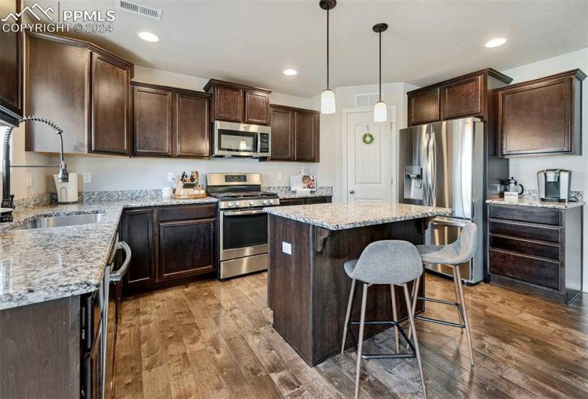 Kitchen featuring appliances with stainless steel finishes, light stone counters, a center island, and hardwood / wood-style flooring