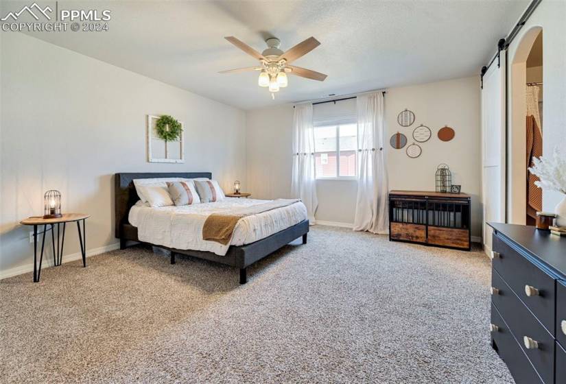 Bedroom featuring a barn door, light colored carpet, and ceiling fan