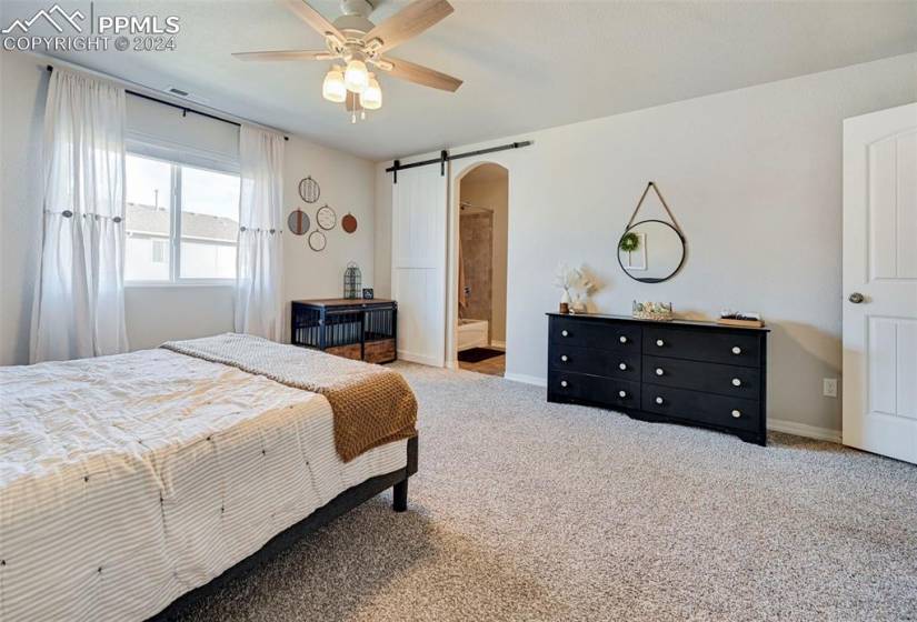 Bedroom with light colored carpet, ensuite bath, ceiling fan, and a barn door