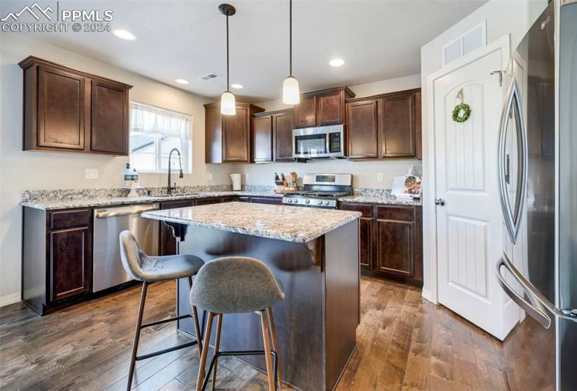 Kitchen featuring a kitchen island, pendant lighting, dark wood-type flooring, appliances with stainless steel finishes, and a breakfast bar area