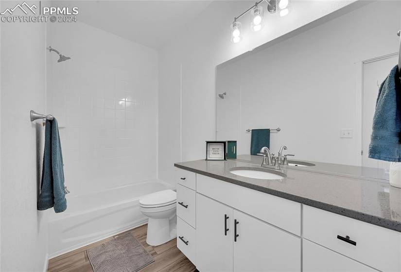 Full main level bathroom with quartz CT's, LVP style floors, toilet, large vanity, and tiled shower / bath