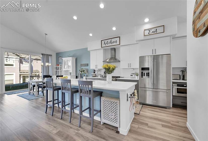 Gourmet kitchen featuring white cabinets, wall chimney range hood, recessed lighting, an island with sink, and appliances with stainless steel finishes