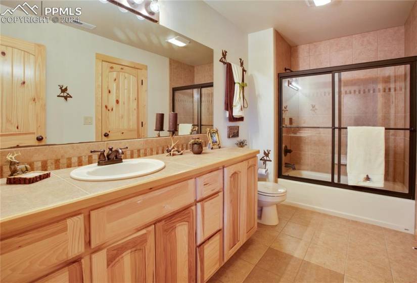 Lower level bathroom featuring single sink, tile flooring, enclosed tub / shower combo, and vanity with extensive cabinet space